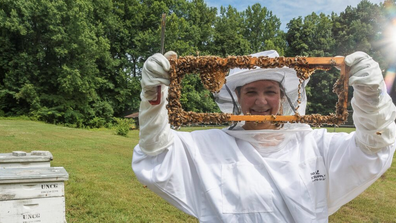 Dr. Kaira Wagoner in a bee suit with part of a hive